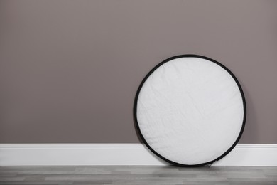 Photo of Professional light reflector near grey wall in room, space for text. Photography equipment