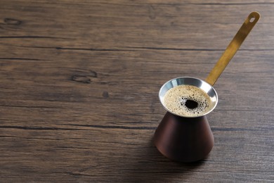 Photo of Turkish coffee pot with hot drink on wooden table, space for text