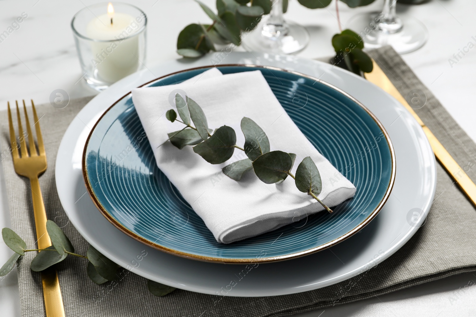 Photo of Stylish setting with cutlery and eucalyptus leaves on white marble table, closeup