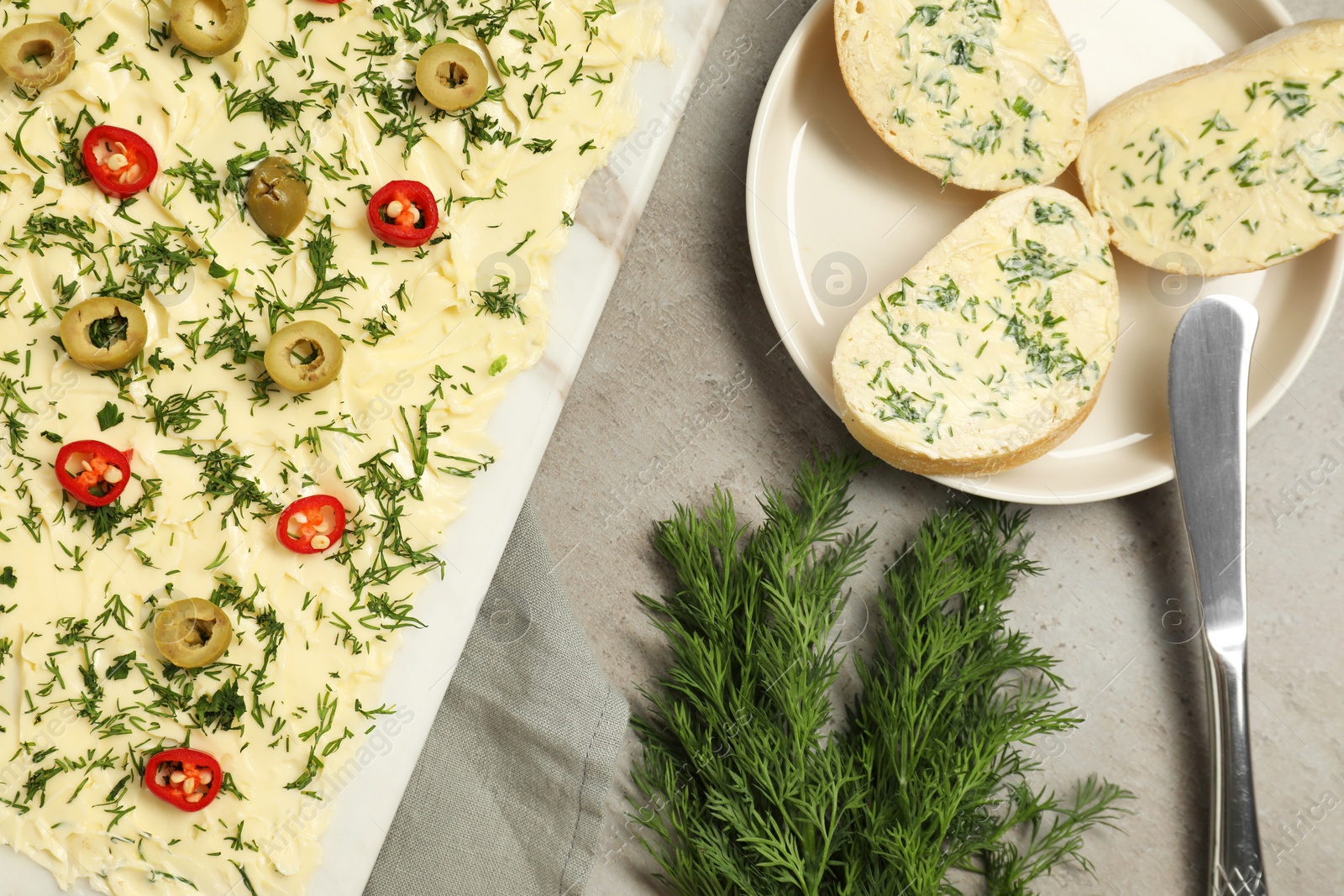 Photo of Fresh butter board with cut olives, dill, bread and knife on grey table, flat lay