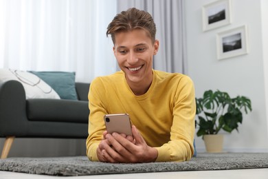 Photo of Happy young man having video chat via smartphone on carpet indoors