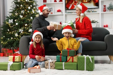 Photo of Happy family in Santa hats with Christmas gifts at home