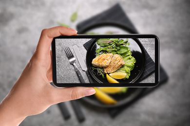 Image of Blogger taking picture of delicious grilled fish at table, closeup. Food photography