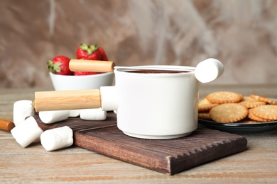 Photo of Fondue pot with chocolate and marshmallow on wooden table