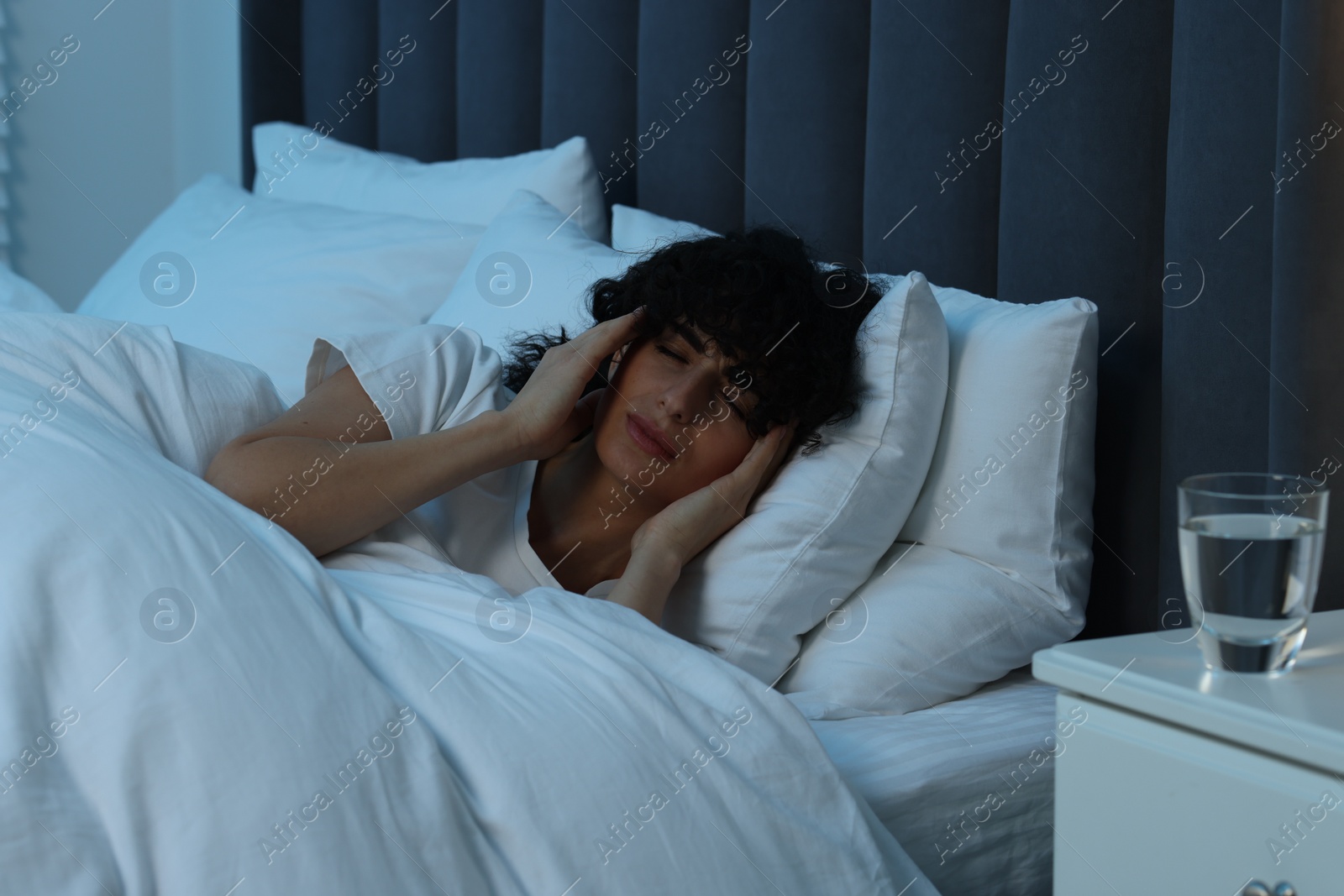 Photo of Young woman suffering from headache in bed at night