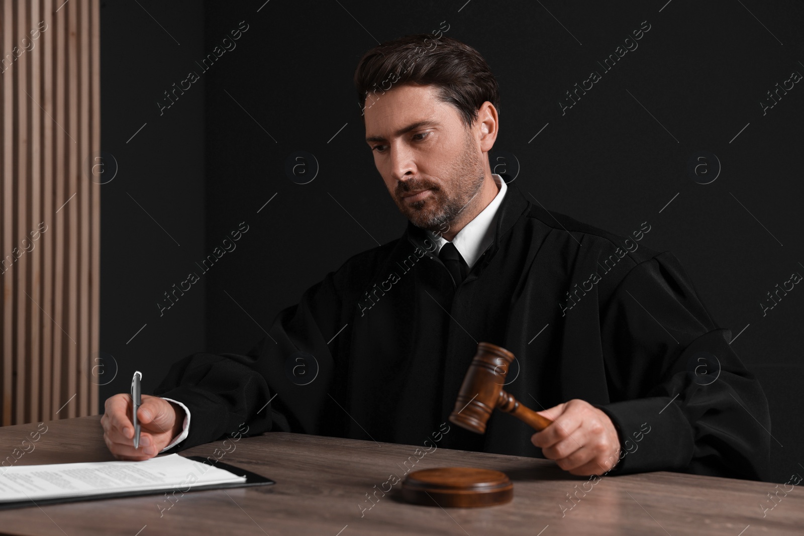 Photo of Judge with gavel and papers sitting at wooden table against black background