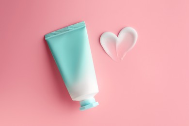 Photo of Tube and sample of facial cream on pink background, top view