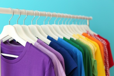 Rack with rainbow clothes on color background