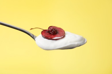 Photo of Spoon with yogurt and cherry on yellow background, closeup