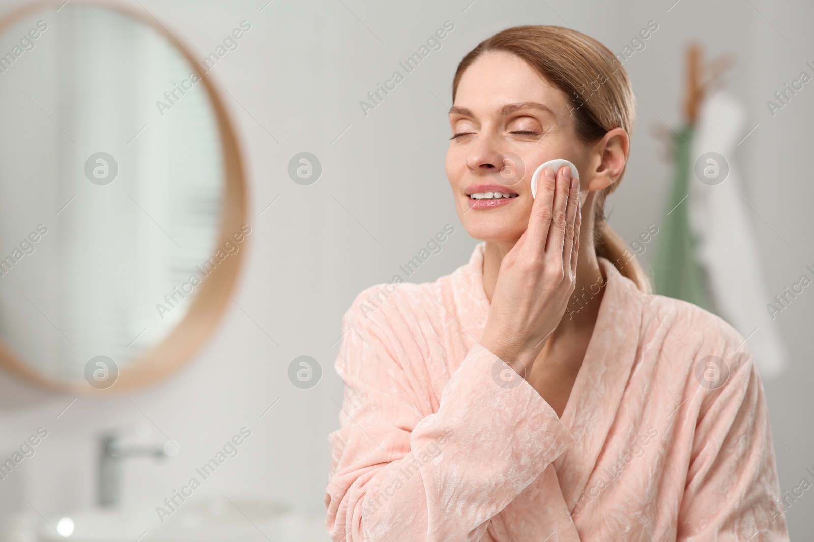 Photo of Beautiful woman removing makeup with cotton pad indoors, space for text