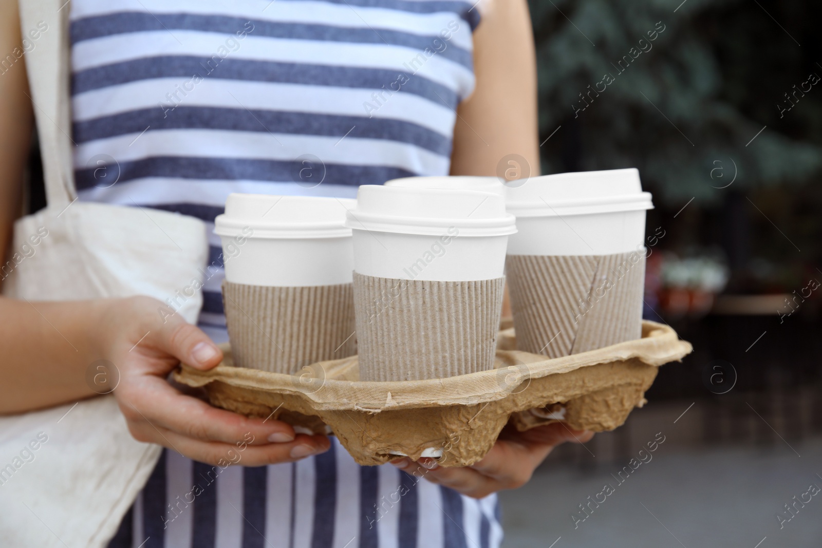 Photo of Woman holding cardboard holder with takeaway paper coffee cups outdoors, closeup