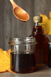 Spoon with tasty maple syrup over jar at wooden table