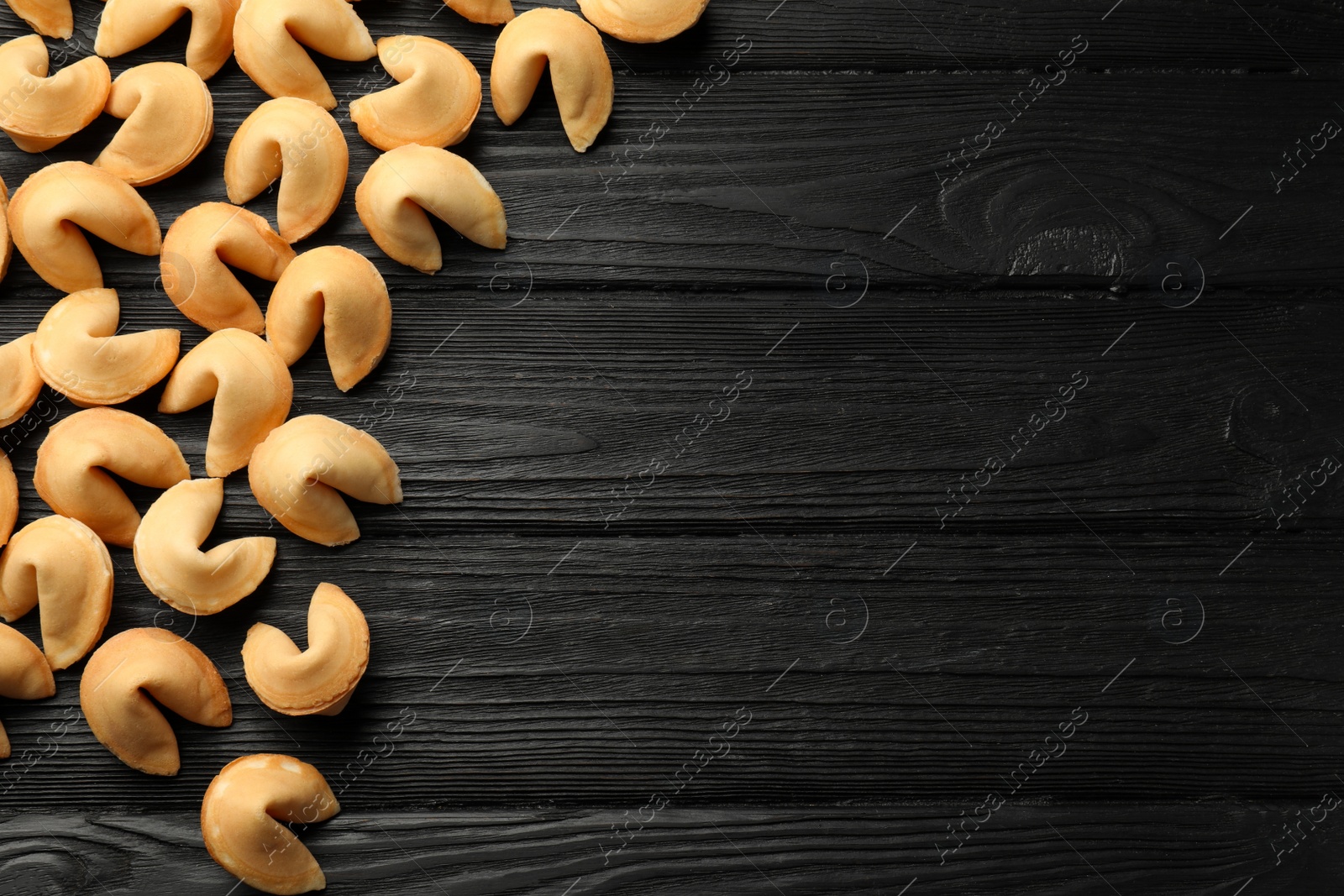 Photo of Tasty fortune cookies with predictions on black wooden table, flat lay. Space for text
