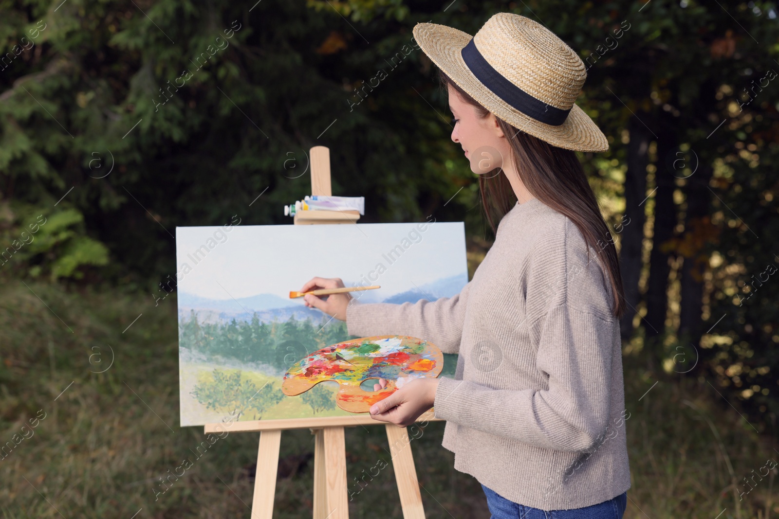 Photo of Young woman drawing on easel with brush outdoors