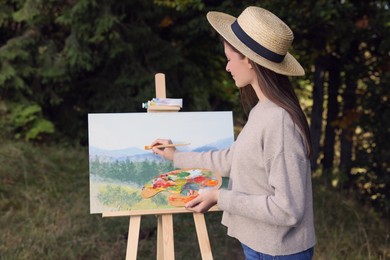 Photo of Young woman drawing on easel with brush outdoors