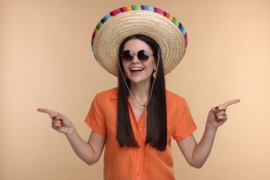 Photo of Young woman in Mexican sombrero hat and sunglasses pointing at something on beige background