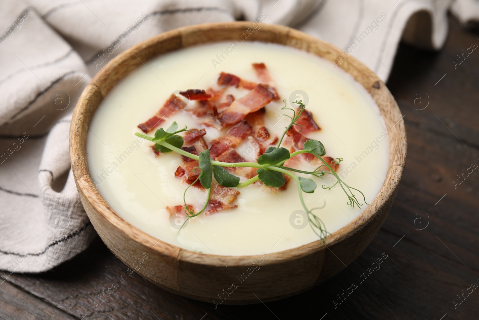 Photo of Delicious potato soup with bacon and microgreens in bowl on wooden table, closeup