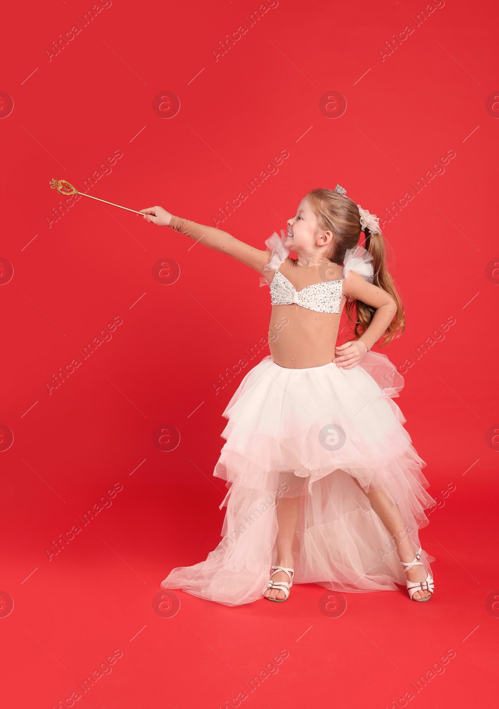 Photo of Cute girl in fairy dress with diadem and magic wand on red background. Little princess