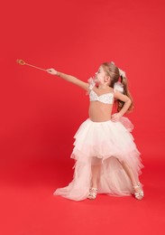 Cute girl in fairy dress with diadem and magic wand on red background. Little princess