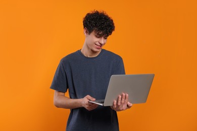 Handsome young man using laptop on orange background