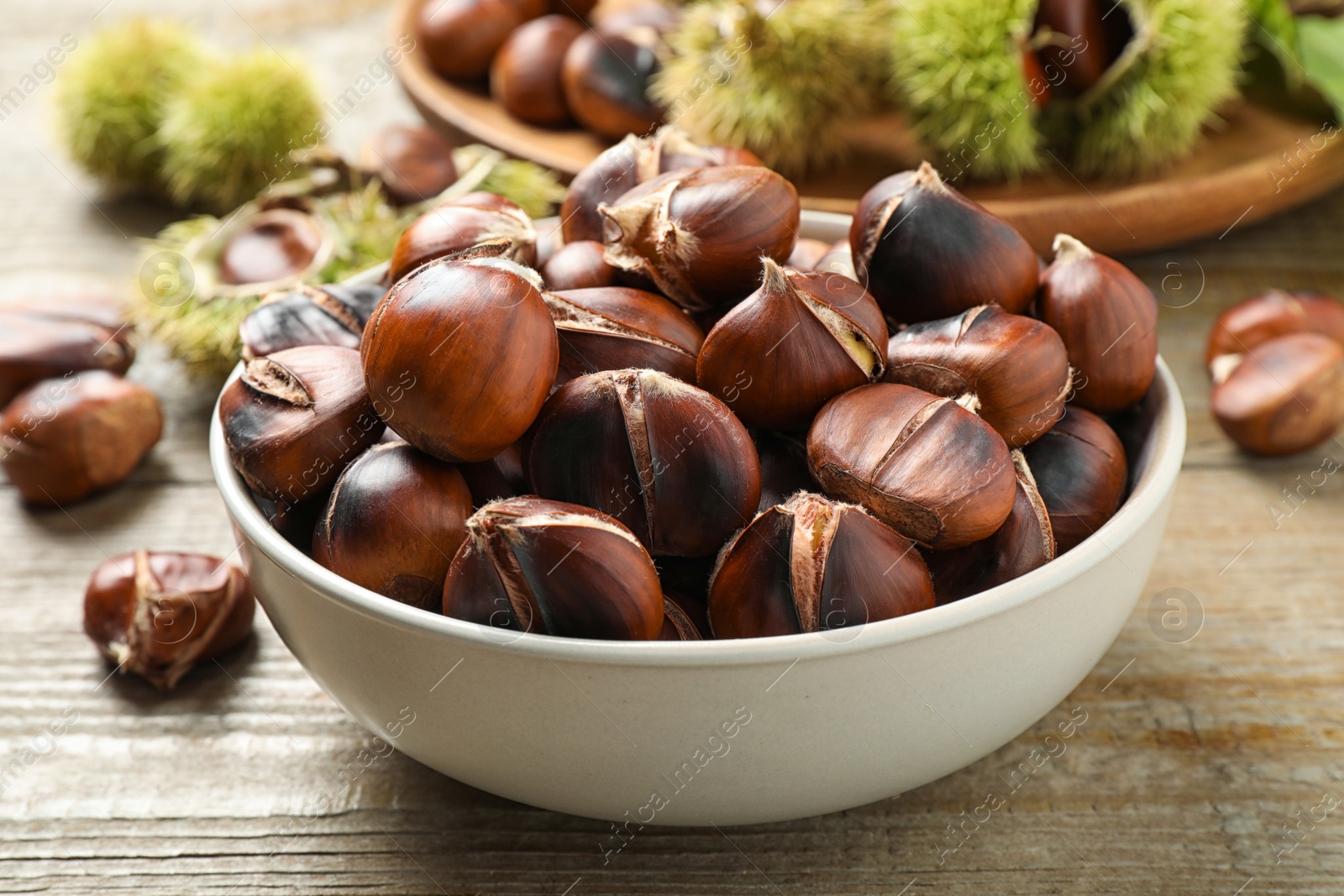 Photo of Delicious roasted edible chestnuts in bowl on wooden table, closeup
