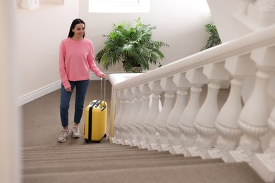 Photo of Beautiful young woman with suitcase going up stairs in hotel