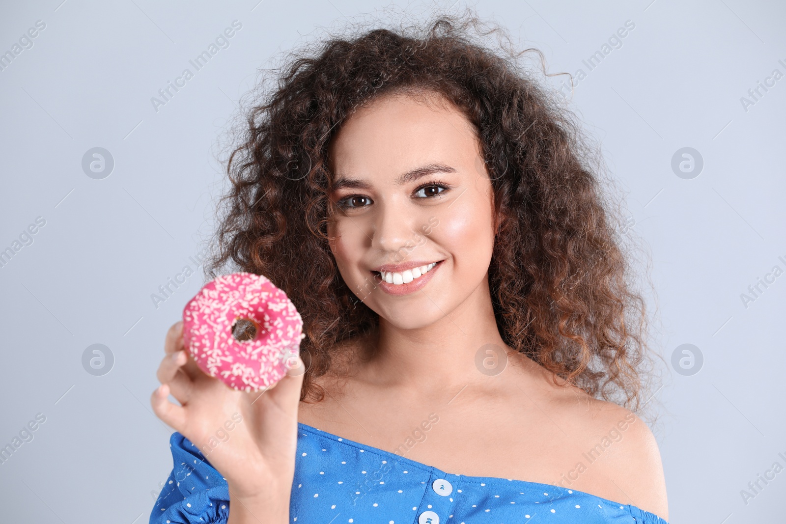 Photo of Beautiful African-American woman with donut on light grey background