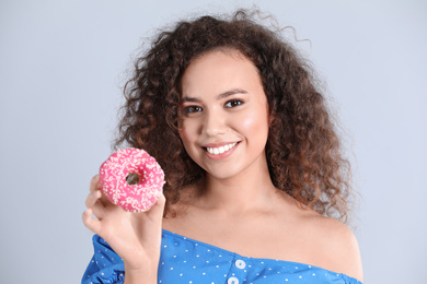 Beautiful African-American woman with donut on light grey background