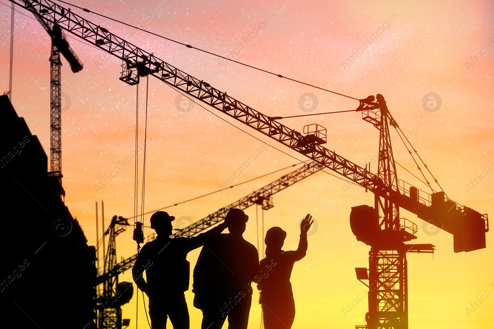 Image of Silhouettes of engineers near construction site at sunrise