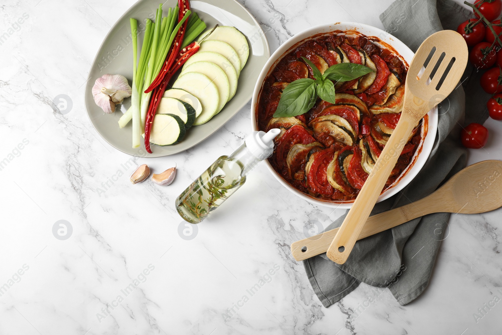 Photo of Delicious ratatouille and ingredients on white marble table, flat lay