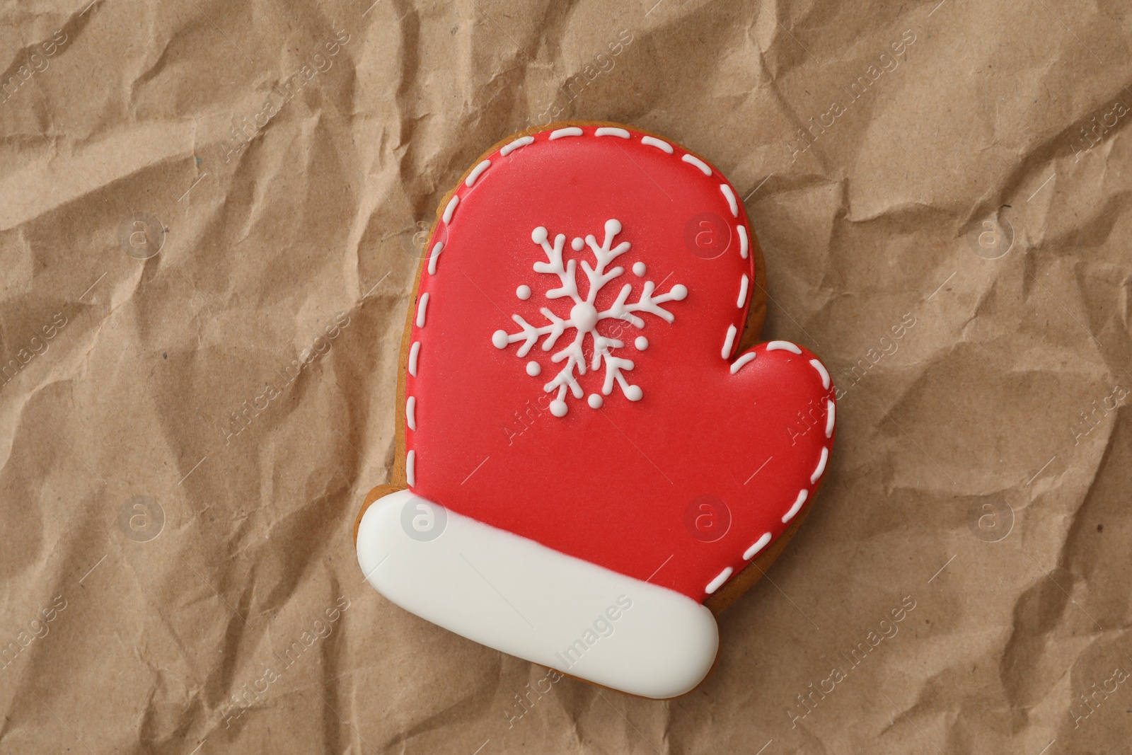 Photo of Christmas mitten shaped gingerbread cookie on crumpled parchment, top view