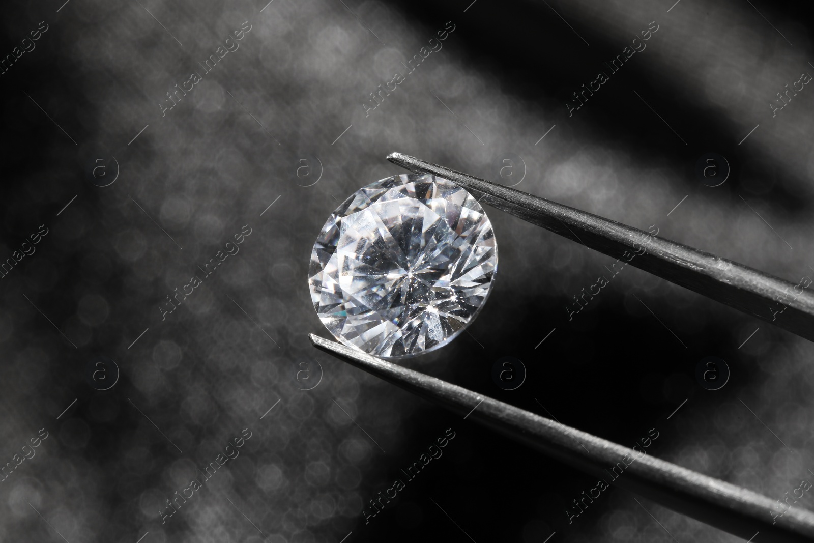 Photo of Tweezers with beautiful shiny diamond on dark background, closeup