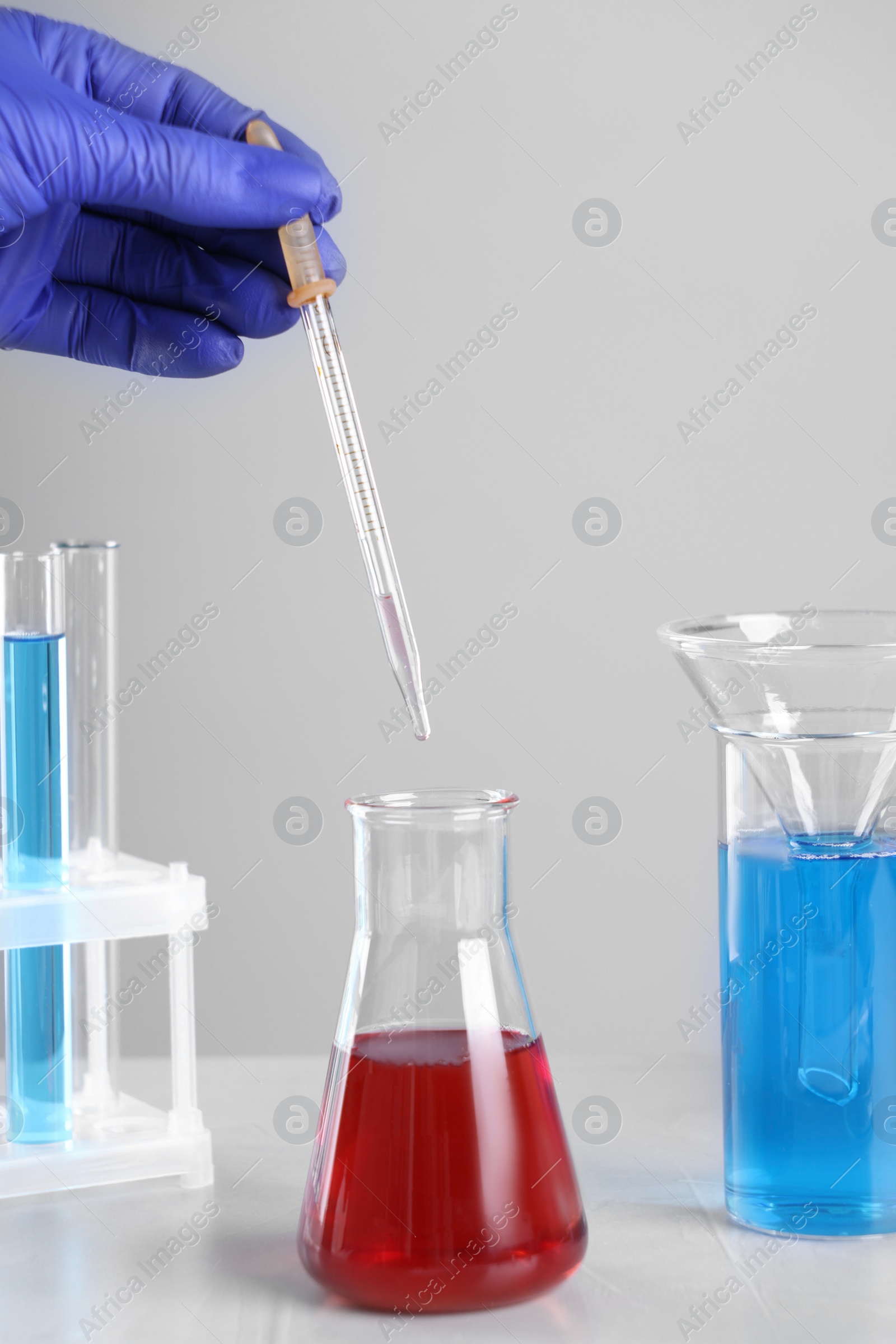 Photo of Scientist dripping liquid from pipette into flask at white table, closeup