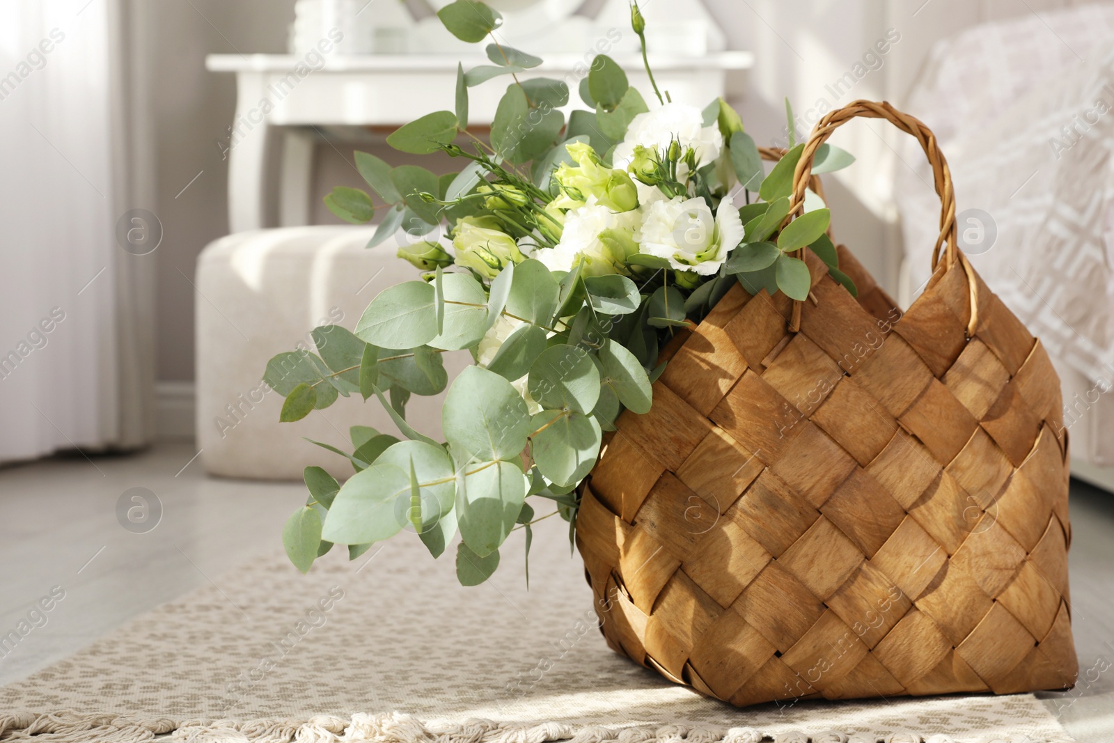 Photo of Stylish wicker basket with bouquet on floor in bedroom