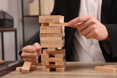 Photo of Playing Jenga. Man removing wooden block from tower at table indoors, closeup