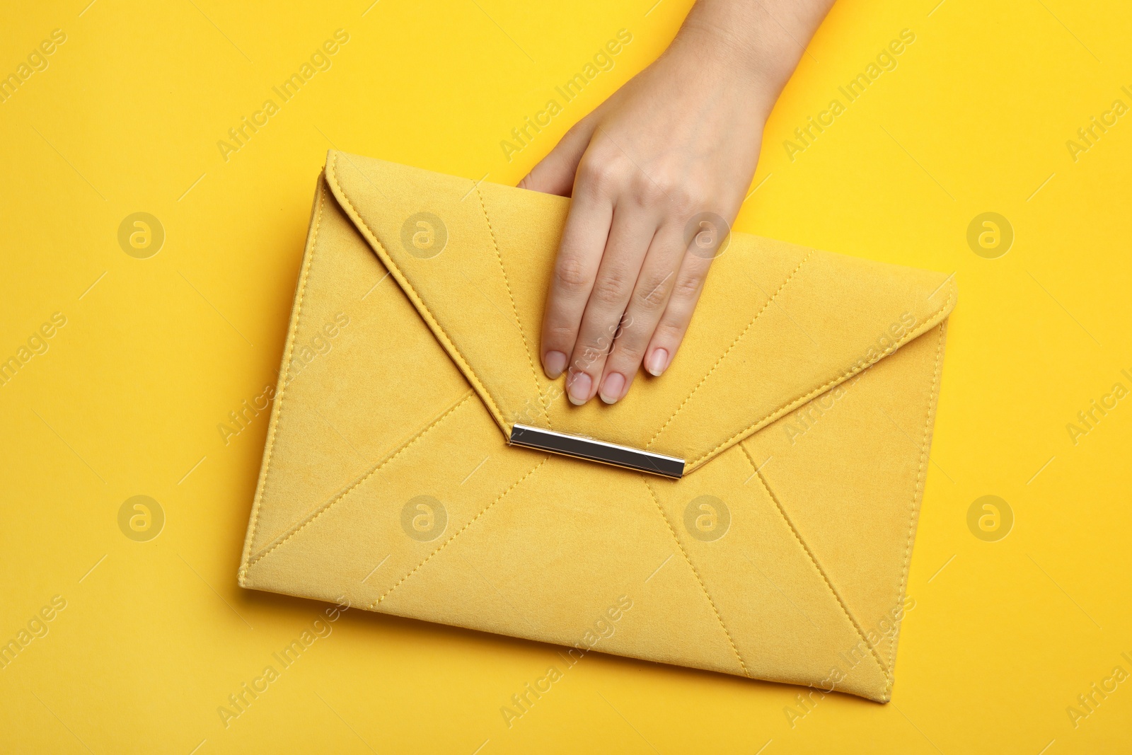 Photo of Woman holding envelope bag on yellow background, top view