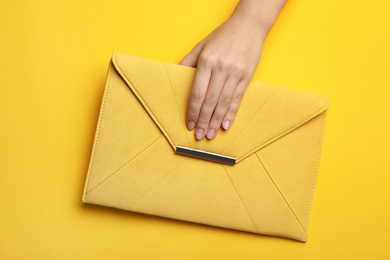 Photo of Woman holding envelope bag on yellow background, top view
