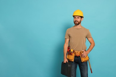 Professional builder in hard hat with tool belt on light blue background, space for text