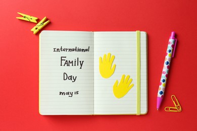 Photo of Notebook with text International Family Day May 15 and stationery on red background, flat lay