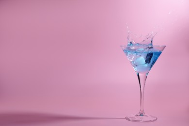 Cocktail splashing out of martini glass on pink background, space for text