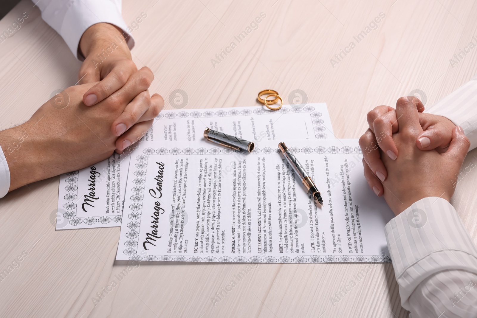 Photo of Man and woman signing marriage contract at light wooden table, closeup