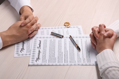 Man and woman signing marriage contract at light wooden table, closeup