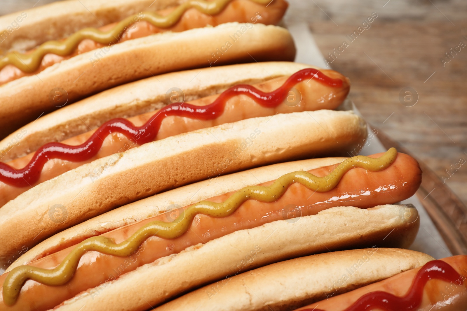 Photo of Tasty hot dogs on wooden board, closeup