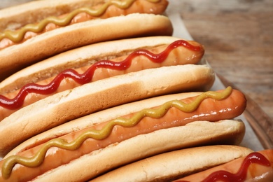 Photo of Tasty hot dogs on wooden board, closeup