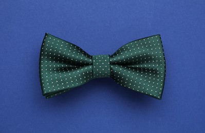 Photo of Stylish green bow tie with polka dot pattern on blue background, top view