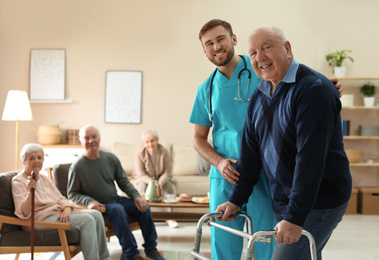 Care worker helping to elderly man with walker in geriatric hospice