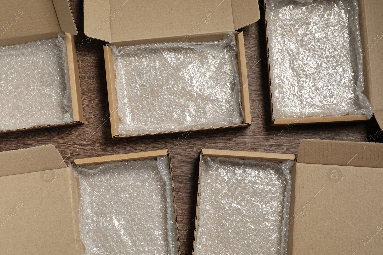 Photo of Many open cardboard boxes with bubble wrap on wooden table, flat lay