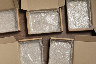 Many open cardboard boxes with bubble wrap on wooden table, flat lay