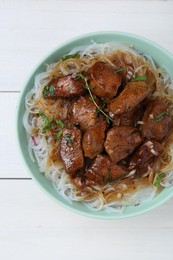 Bowl with pieces of soy sauce chicken and noodle on white wooden table, top view