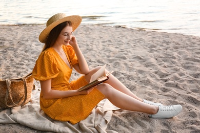 Photo of Young woman reading book on sandy beach